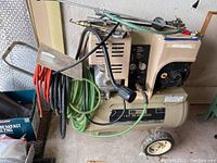 Side view of the beige Sears Craftsman air compressor with attached hoses and tools, showing overall condition and size.