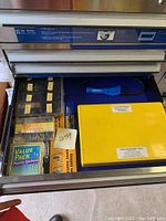 Top drawer photo showing various stored items including a blue handled tool, yellow plastic organizer boxes, and boxed items labelled as screw and anchor kits