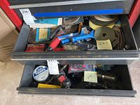 Two metal drawers containing sanding discs, hand tools including a screwdriver with blue handle, tape, and small hardware items