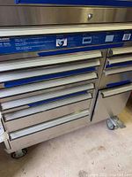Full view of stainless steel drawer unit with blue handles on wheels.