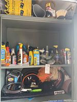 Shelving cabinet showing many bottles and cans of vehicle cleaning liquids and maintenance sprays, brushes, and some automotive accessories.