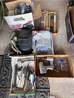 Top-down image showing multiple boxes with welding helmets, gloves, metal rods and flux, and pneumatic tools along with smaller hand tools spread in trays.