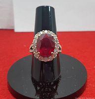 Front view of ring on black display stand showing halo and ruby center
