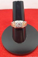 Front view of ring on black stand showing bezel-set diamond and two-tone gold shoulders