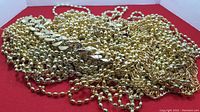 Pile of various gold-colored beads and fake gold chains on a red surface photographed from above.