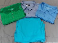 Three golf shirts in green, light blue, and patterned blue-white laid flat next to a pair of light blue golf shorts.
