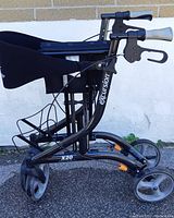 Side view of black Excursion X20 roller walker showing frame, hand brakes, seat, and wheels.