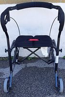 Full front view of a black roller walker showing its frame, wheels, seat and hand brakes.