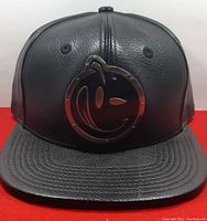 Front view of black leather-textured hat with metal smiley face logo.
