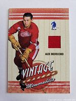 Front of card showing Alex Delvecchio in Detroit Red Wings uniform and embedded red jersey swatch.