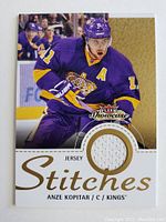 Full front view of the hockey card showing Anze Kopitar in purple LA Kings jersey holding a hockey stick with a built-in fabric patch from his game worn jersey.