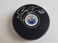 Top view of black hockey puck with autosigned silver ink Connor McDavid signature and number 97 above Edmonton Oilers logo.
