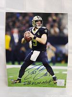 Glossy 8x10 photo of Drew Brees in Saints uniform holding a football, signed and inscribed with "SB XLIV MVP." Shows official NFL hologram for authenticity.