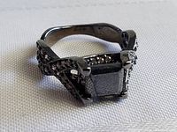 Front angle showing the square-cut black central stone and accent stones on the prongs and band.