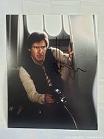 Signed 8x10 photo showing Harrison Ford as Han Solo holding a blaster, signed in black ink.