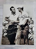 Full view of the dual signed black and white photograph showing Jack Nicklaus and Arnold Palmer shaking hands with signatures visible.