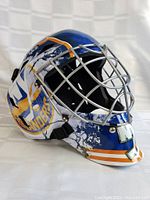 Front-left angled view of the blue goalie mask featuring New York Islanders logo and a silver metal face cage.