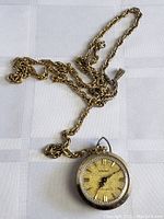 Photo showing full stopwatch pendant attached to gold-tone linked chain, lying on white cloth.