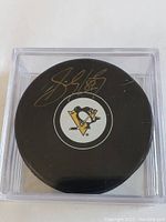 Front view of the hockey puck showing the Pittsburgh Penguins logo and Sidney Crosby signature in gold ink inside a clear protective case.