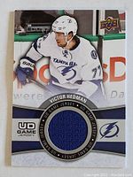 Front of Victor Hedman NHL trading card showing player image and embedded blue jersey fabric patch.