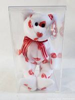Front view of the white and red lip print Beanie Baby encased in a clear display box.