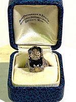 Ring displayed in blue textured box with cream velvet interior; retailer’s name stamped on lid