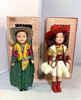 Front view of both cowboy and cowgirl dolls standing in front of their original pink decorative boxes.