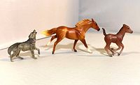Three Breyer Reeves 1990s collectible animal figurines: large chestnut horse, smaller foal, and grey wolf all arranged on white background.