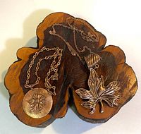 Two coppertone-tone necklaces displayed on carved wooden holder, one with round leaf medallion and one with large leaf pendant