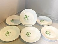 Photo of six white Corelle dessert plates with green vintage Mickey Mouse design arranged on a surface with one plate displayed upright on a stand