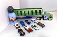 Photo shows green and gray Hot Wheels motocross transport truck with trailer, eight assorted Hot Wheels cars, and a blue Hot Wheels water bottle with black cap on white background.