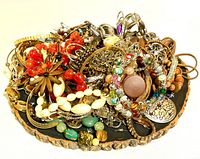 Top-down photo showing assorted jewelry items including colorful beaded bracelets, metal chain necklaces, earrings, and decorative pins placed on a round wooden display base.