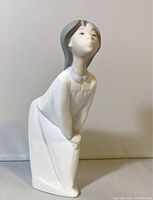 Front angled view of the porcelain figurine showing the girl leaning forward with lips pursed.