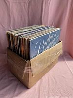 Box of LP vinyl records showing multiple record sleeves inside a cardboard box secured with tape.