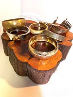 Six metal bracelets displayed on wooden block showing variety of styles and gold/copper tones