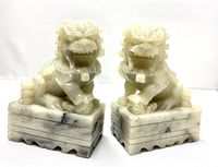 Front view of the pair of carved stone Foo dogs showing detailed carving, open mouths and seating posture on rectangular bases.