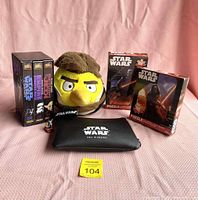 Star Wars VHS tapes, Angry Birds Han Solo plush, United Airlines amenity kit pouch, Kinder Flynn figure, and Disney Star Wars puzzles arranged on pink fabric background.