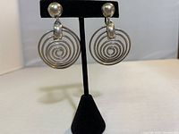 Front view of the sterling silver spiral earrings featuring ball studs and circular spiral drops hanging below, displayed on black mount.