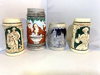 Front view of all four vintage German ceramic steins showing varied heights and intricate relief designs.