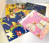Eight vintage wrapping paper packs displayed, featuring Power Rangers and Barbie prominently, with other assorted vintage designs behind them