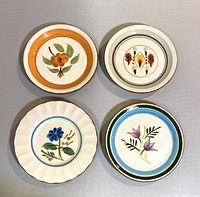 Four vintage Stangl bread and butter plates showing the distinct floral patterns: orange Bittersweet, amber leaf Amber Glo, blue flower Bachelors Button, and purple flower with blue/green rim.