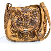 Front view of the vintage brown leather tooled shoulder bag showing detailed floral embossing and turn-lock closure.