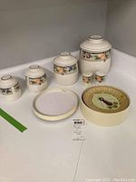 Full view of set including Mikasa canisters, salt and pepper shakers with fruit border design, and Pottery Barn Bee Brie ceramic plate with lid.