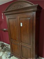 Front view of large wooden armoire with two doors closed, showing overall shape, wood finish, and handles.