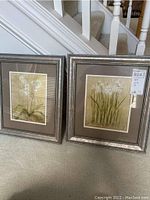Pair of two framed floral prints shown side by side on carpeted floor near stairs.