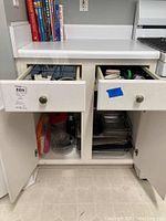 View of white kitchen cabinets with two drawers open revealing various kitchenware items inside.