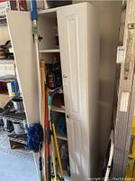 Photo of the white wooden storage cabinet showing the single door slightly open and cleaning tools stored nearby.