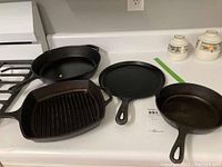 Overview of four cast iron pans on a kitchen stove, showing their shapes and sizes.