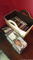 Photo showing a tan woven straw basket filled with a large number of CD jewel cases, some CDs laid out in front of the basket. Visible CDs include Bob Dylan, Rod Stewart, Neil Young.