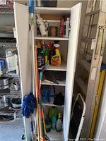 Wide view of white cabinet with multiple shelves filled with cleaning supplies and tools including mop and bucket inside cabinet